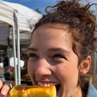 A woman biting a honey-glazed grilled cheese skewer at a farmers market (illustrative photo)