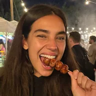 A young woman biting a sausage skewer at a night market (illustrative photo)